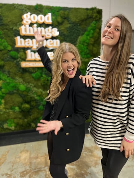 An image of two women in front of a moss wall.